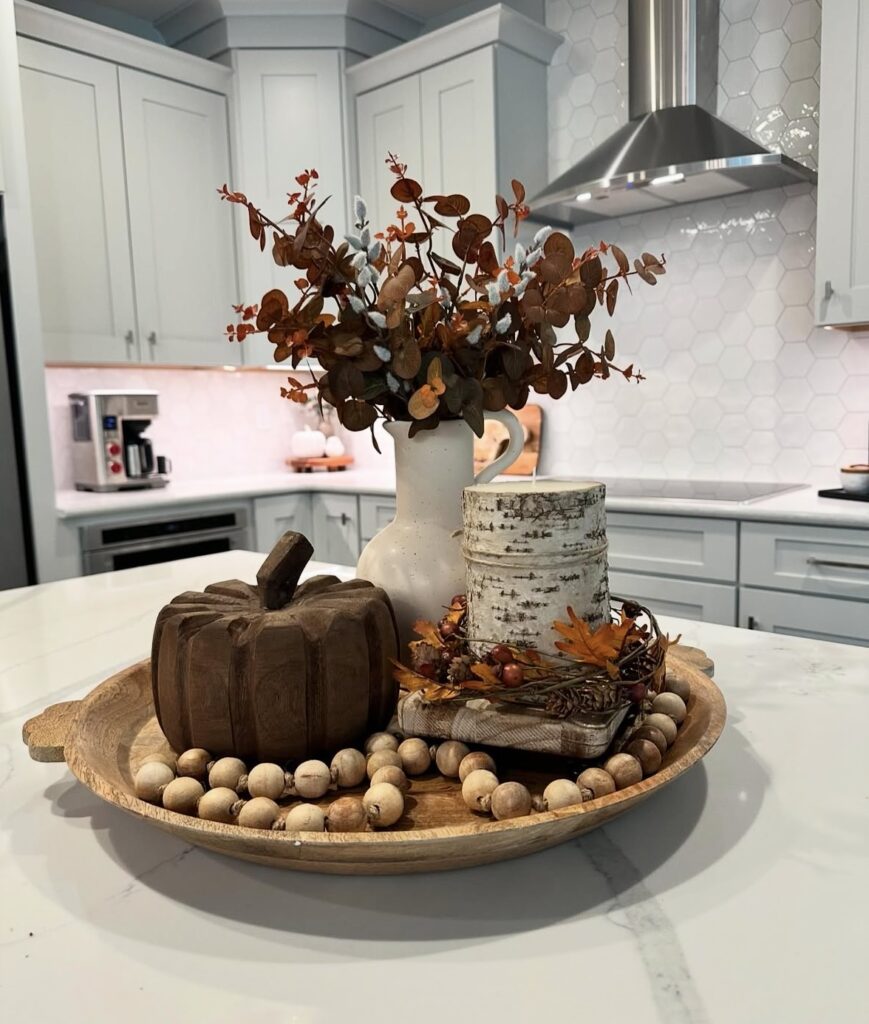 Wooden tray with white vase of orange foliage, wood pumpkin, candle wrapped in birch bark, and wood bead garland