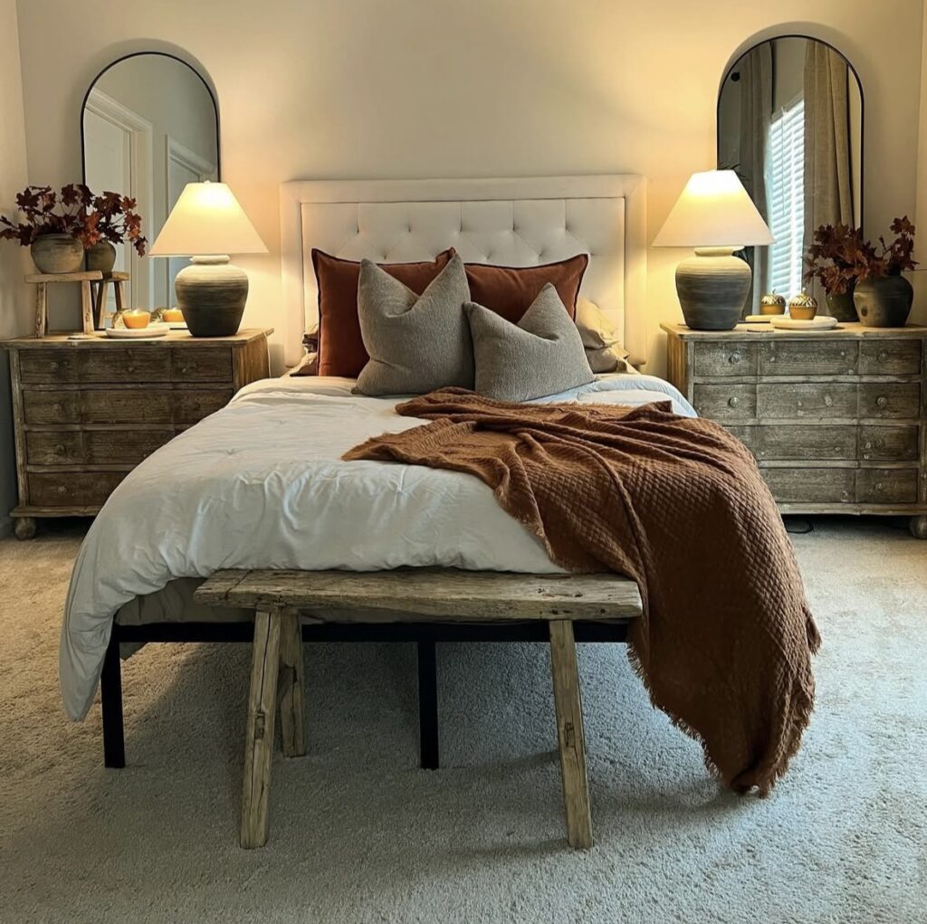 Minimal rustic fall bedroom with neutral walls, white bedding, orange throw blanket, and matching pillows, with a weathered wood bench at the foot of the bed.