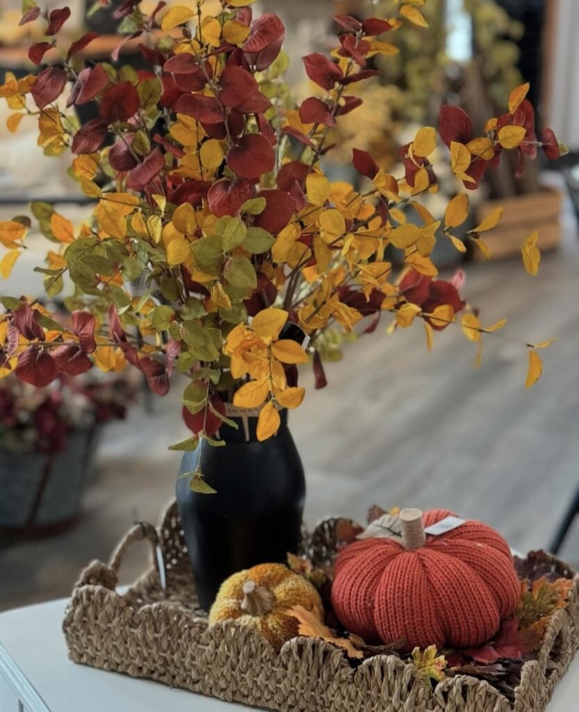 Woven tray with black vase of red and yellow leaves, knit pumpkin, and decorative gourd
