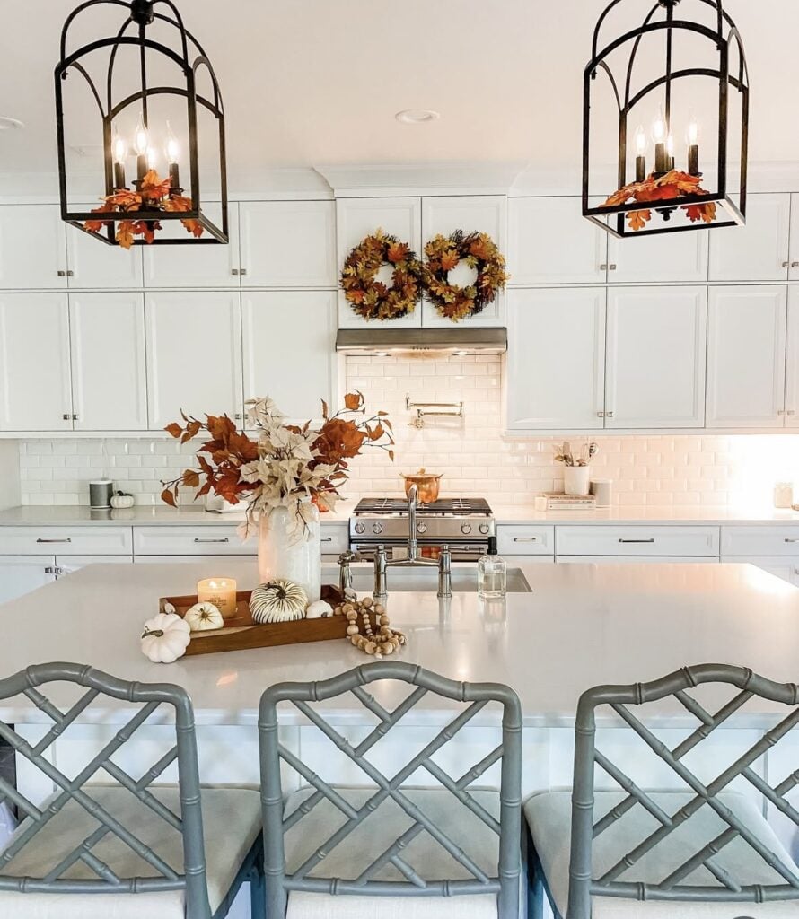 Large kitchen island with wooden tray centerpiece of orange and cream pumpkins, autumn foliage, candle, and beaded garland.