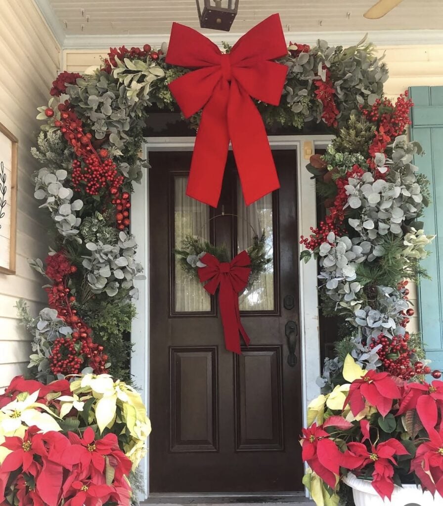 Christmas porch styling with red bow, red poinsettas, with berries and greenery