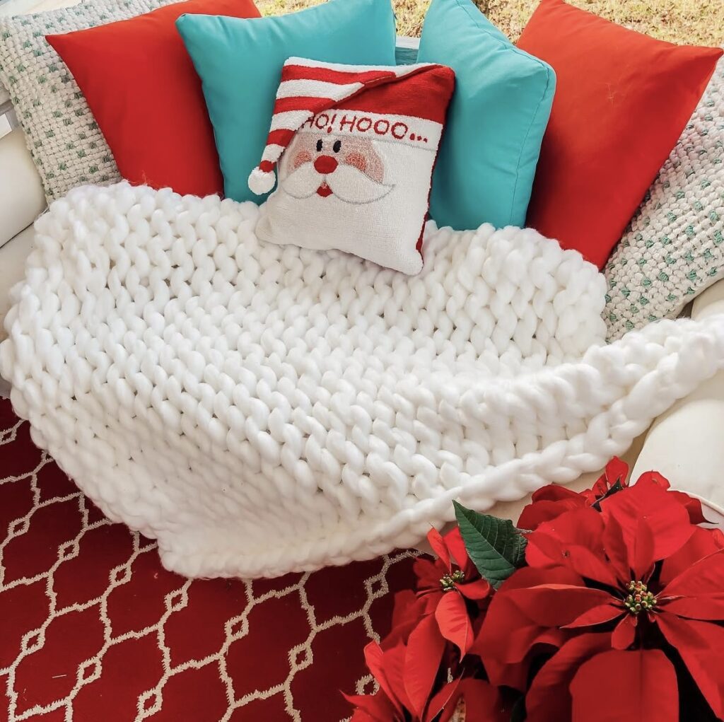 Inviting porch swing decorated for Christmas with red and turquoise accent pillows, a Santa pillow, soft throws, and twinkle lights for a snug holiday nook