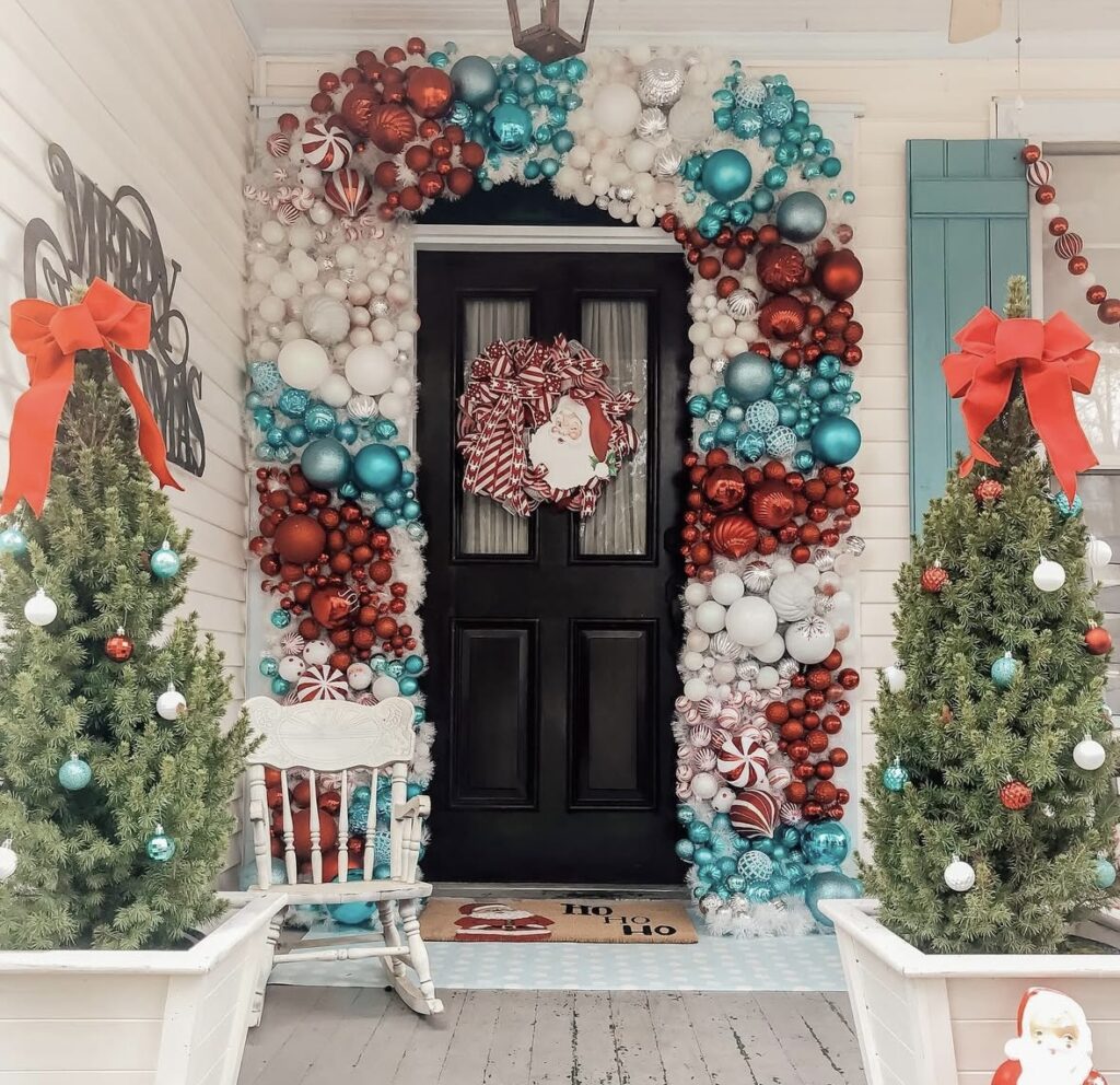 Modern ornament garland in red, white, and aqua around a black door with a Santa wreath and matching potted mini trees
