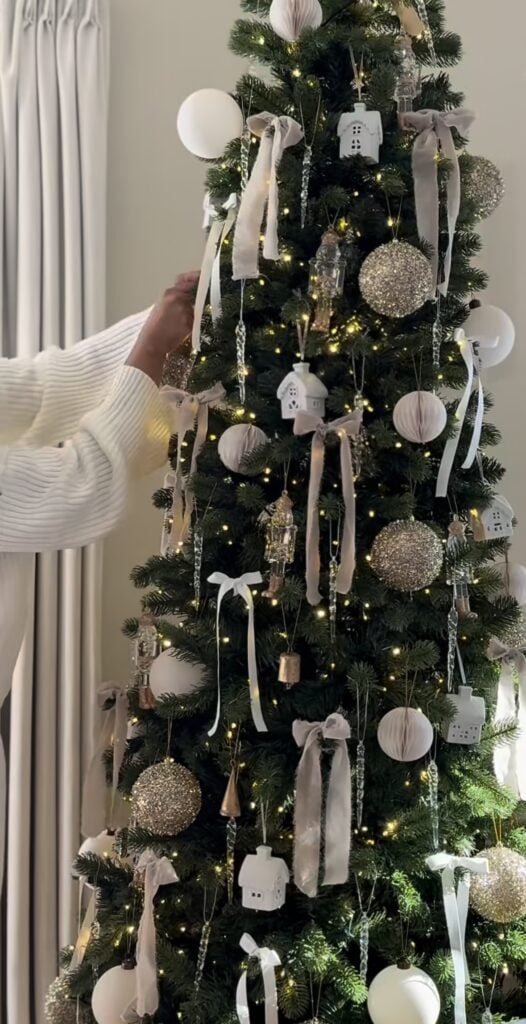 closeup of hands adjusting velvet and gauze bows with glitter ornaments, paper honeycomb baubles, mini house ornaments, crystal icicles