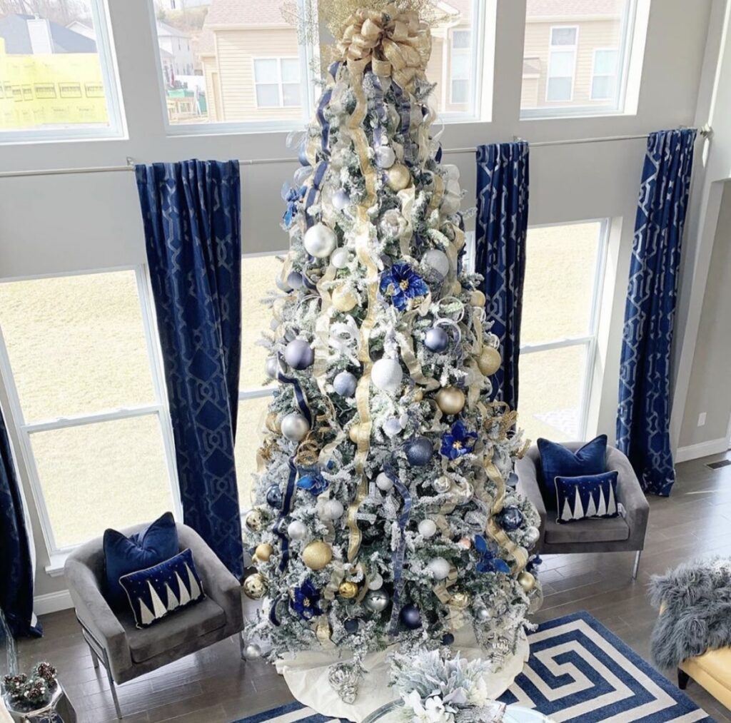 Tall glam Christmas tree in blue and gold with velvet ribbon and luxe ornaments creating a dramatic living room statement.