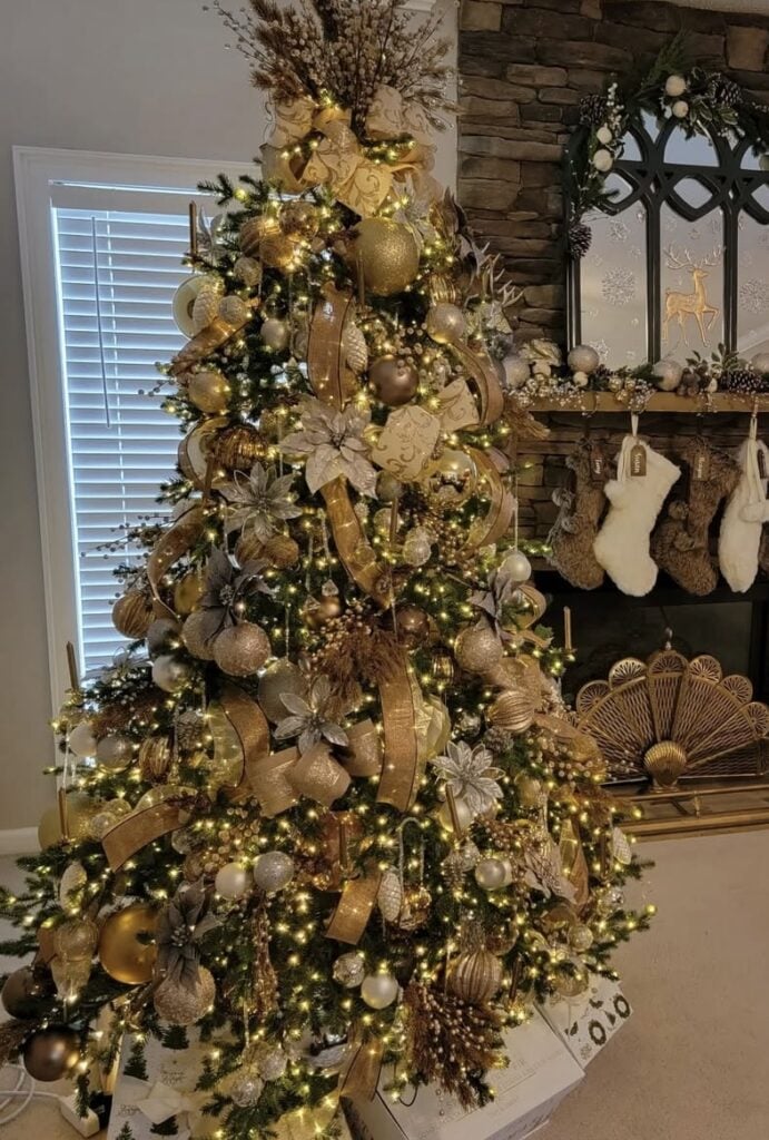 Champagne-gold glam Christmas tree with layered ribbon beside a traditional fireplace.