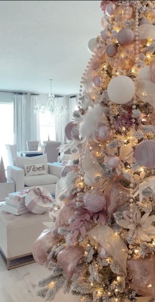 Blush pink-and-white glam Christmas tree with soft feathers, flocked branches, and delicate metallic ornaments for a romantic, airy look