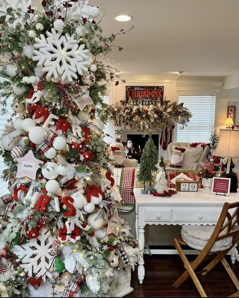 Cozy farmhouse-glam Christmas tree with white and red ornaments, snowflakes, “Merry” signs, and layered ribbon.