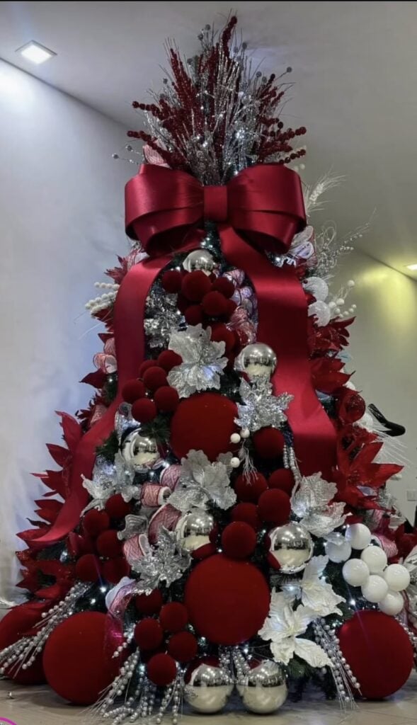 Statement glam Christmas tree with a giant red bow topper, silver poinsettias, and velvet baubles.