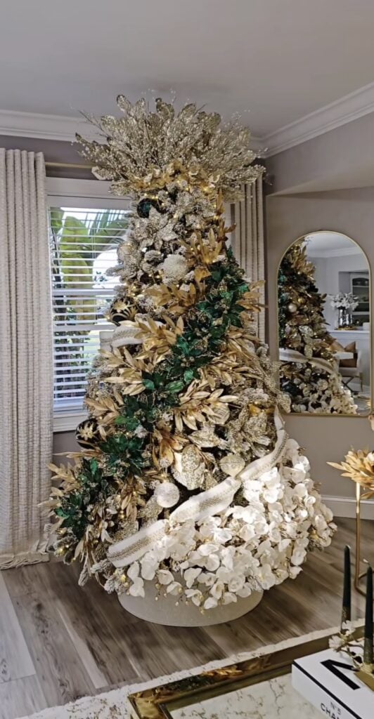 Grand luxury glam Christmas tree with gold and emerald leaves, white orchids, and layered metallic ornaments.