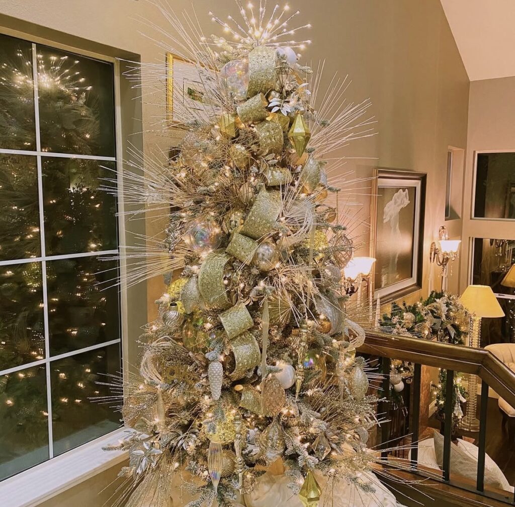 Gold starburst sprays and iridescent ribbon on a luxe glam Christmas tree with layered ornaments.