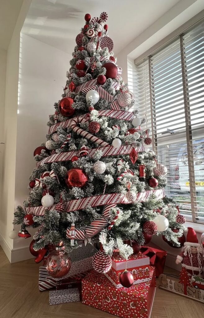 Peppermint-stripe glam Christmas tree with bold red ornaments on a flocked base and candy-cane ribbon.
