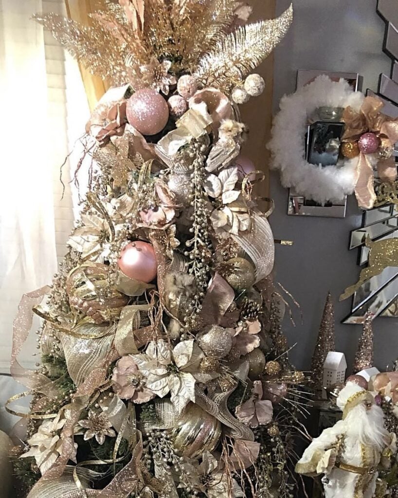 Rose-gold and blush glam Christmas tree with floral picks, sparkle sprays, and shimmering ribbon.