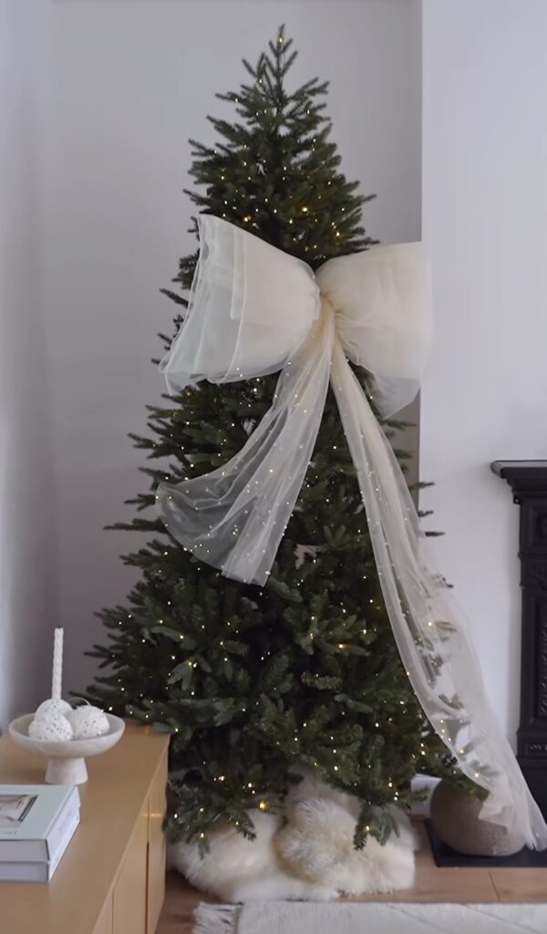 minimalist tree with oversized ivory bow and sheer organza tails, micro lights, neutral scandi room, white faux fur skirt