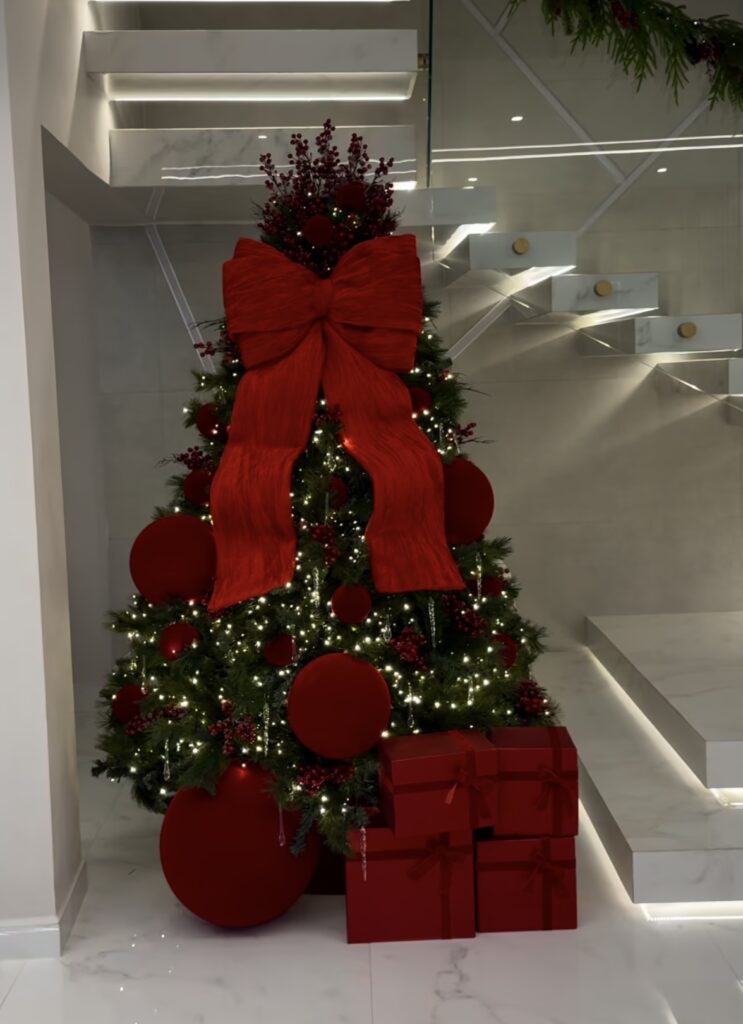 modern minimal Christmas tree with monochrome red bow topper beside a sculptural staircase