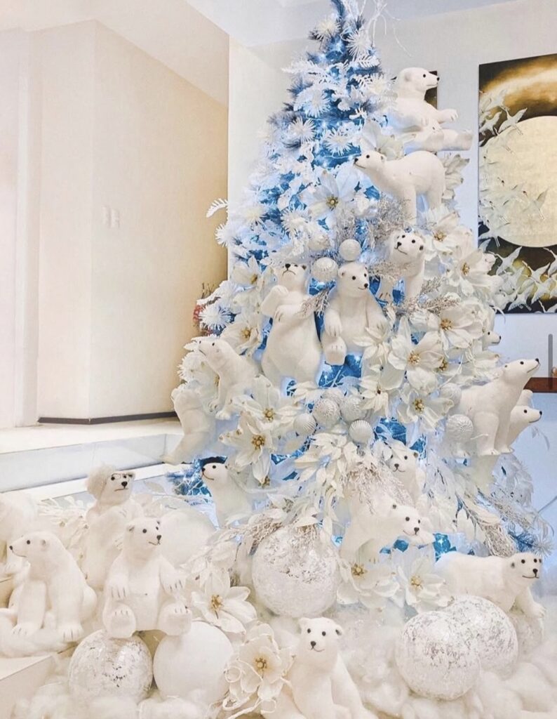 Winter wonderland Christmas tree with all-white flocked branches, icy blue glow, white poinsettias, snowball ornaments, and a faux snow base