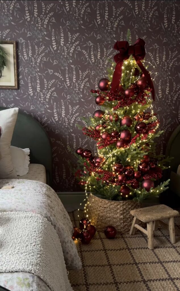 small classic bedroom Christmas tree with red ornaments, bow garland, and cozy fairy lights