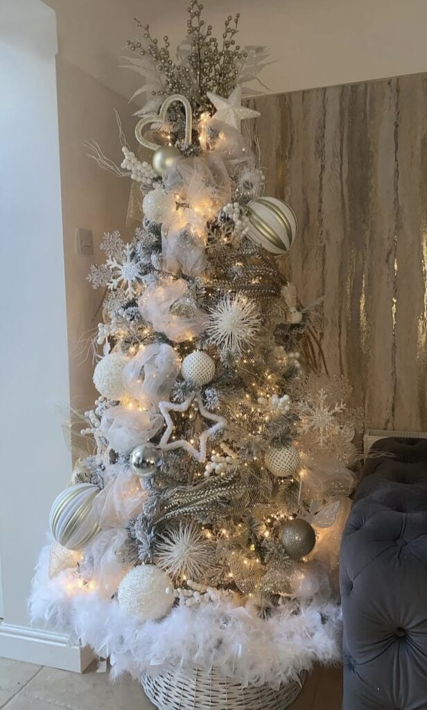 Snowy white-gold-silver glam Christmas tree with mesh ribbon, tulle, feather picks, starburst ornaments, striped baubles, and feather tree skirt.