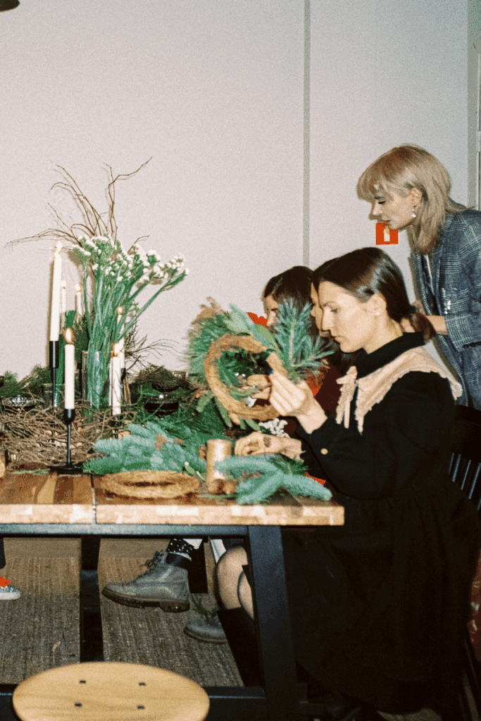 Image of women sitting at a wooden table putting together winter garland