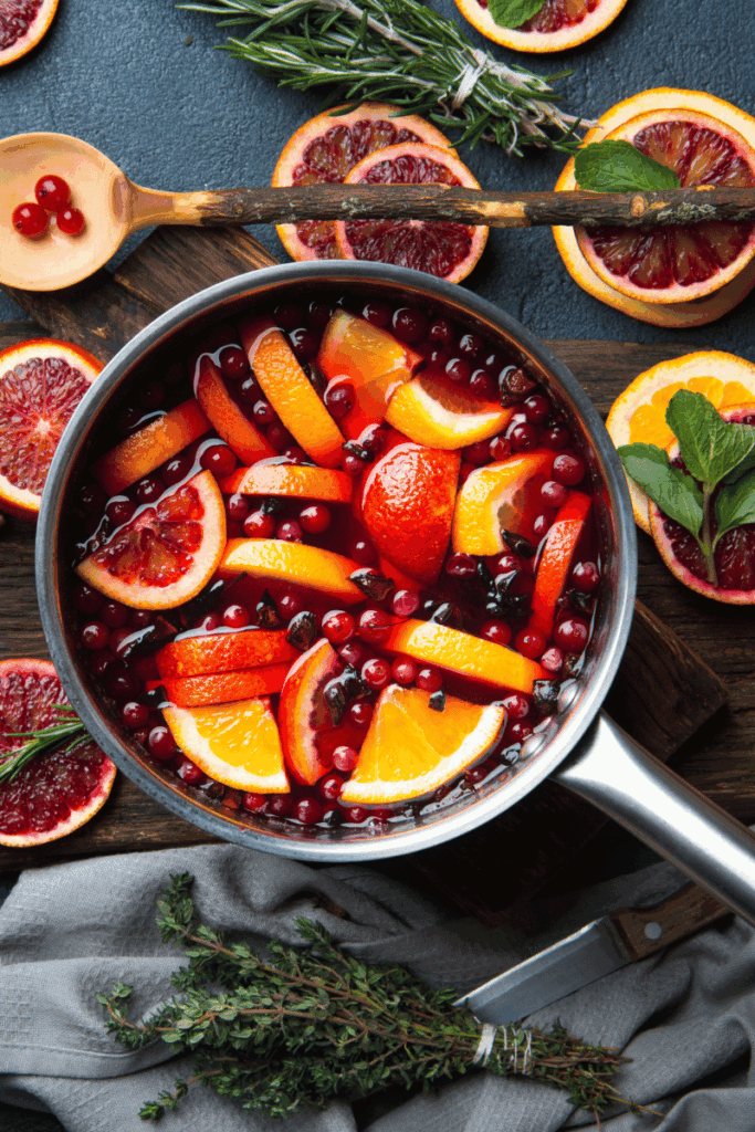 rich image of oranges, cranberries and greenery in a pot to simmer