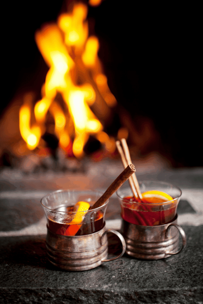 Image of a campfire in the background with warm cider drinks with dried oranges and cinnamon in the foreground