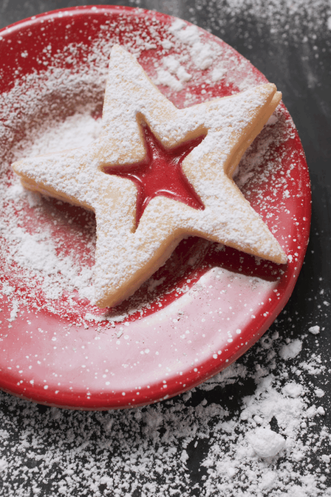 Image of star cookie on a red plate with powdered sugar on the plate and table around it