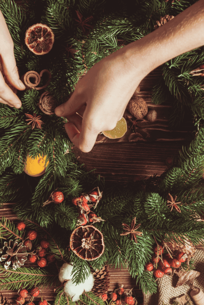A person's hands putting together a wreath with dried oranges, berries, and other symbols used during winter solstice as winter solstice celebration ideas
