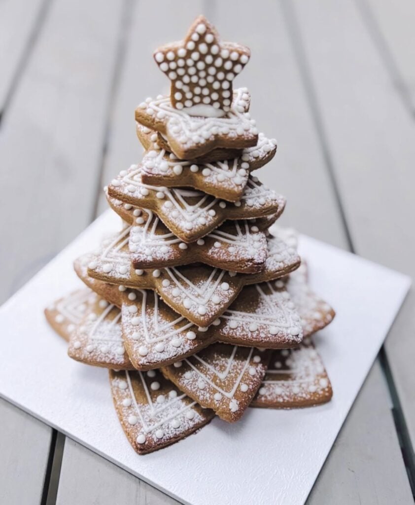 Close-up of a gingerbread Christmas cookie tree stacked on a cake stand, decorated with white icing details and tiny star cookies.