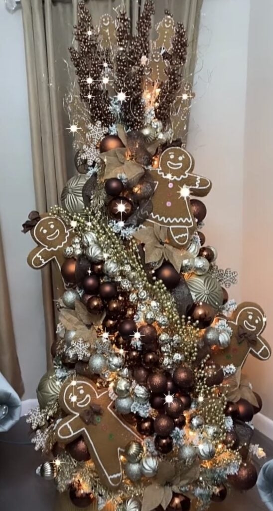Gingerbread-inspired Christmas tree decorated in deep brown and gold ornaments with cookie cutouts and sparkling ribbon.