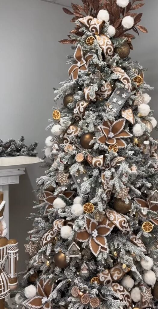 Flocked gingerbread Christmas tree with copper ribbon, dried orange slices, and neutral cookie ornaments for a warm bakery-style look.