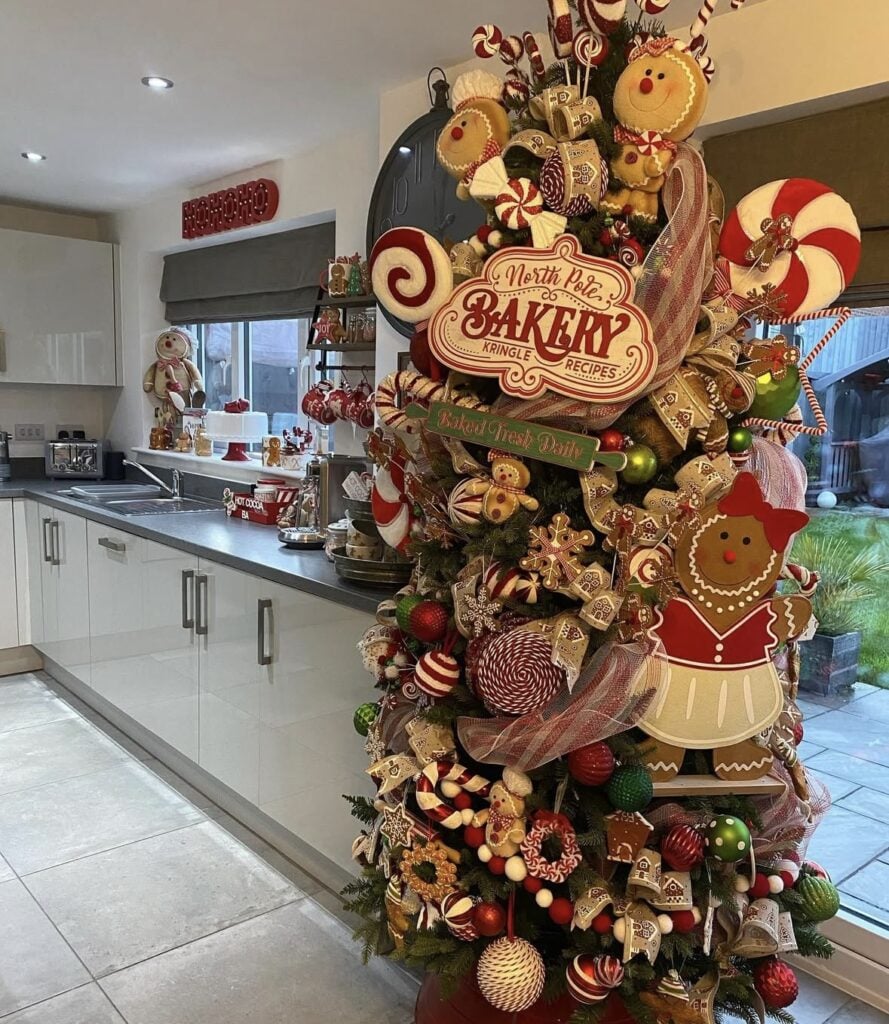 Gingerbread bakery kitchen Christmas tree with red and white ornaments, cookie garlands, and peppermint accents by a festive countertop.
