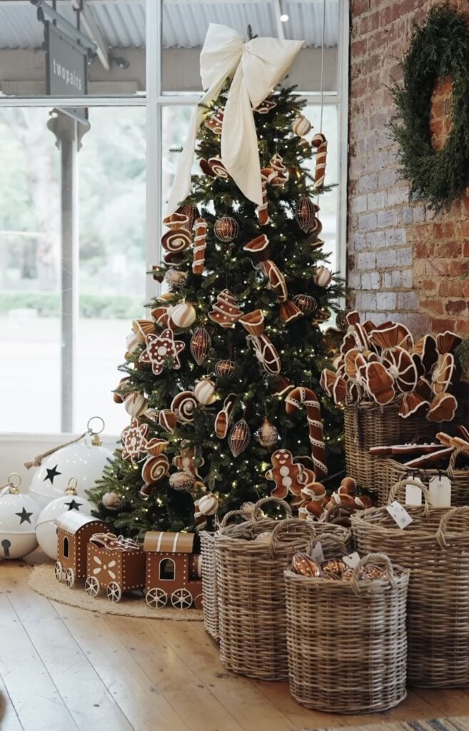 Gingerbread shop display Christmas tree with cookie ornaments, toy train at the base, and candy-inspired decor.
