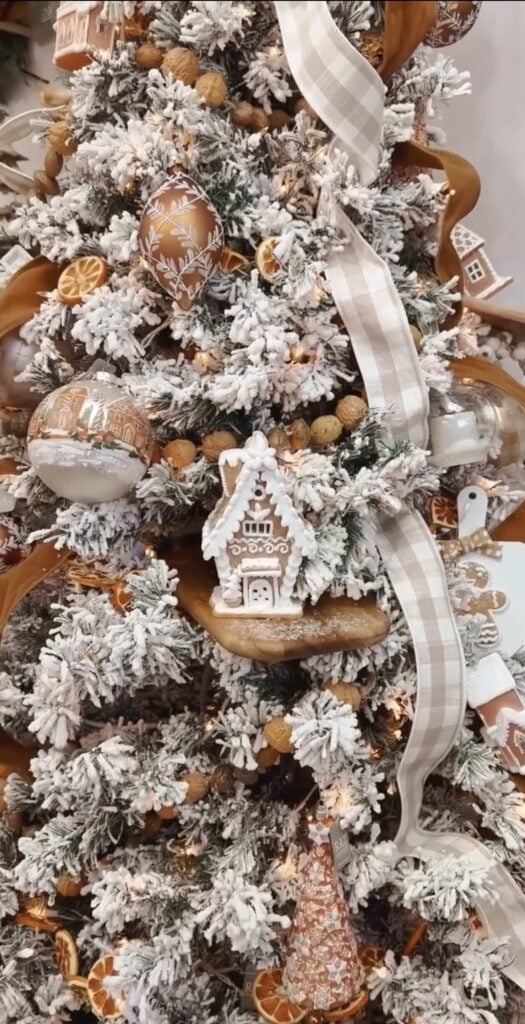 Flocked gingerbread Christmas tree with warm copper and cream ornaments, dried orange slices, and soft ribbon for a cozy bakery feel.