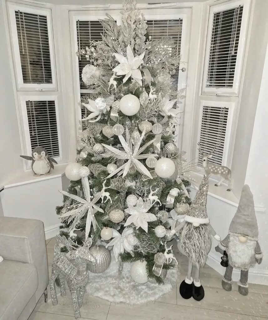 Christmas tree in front of windows decorated in white and silver 