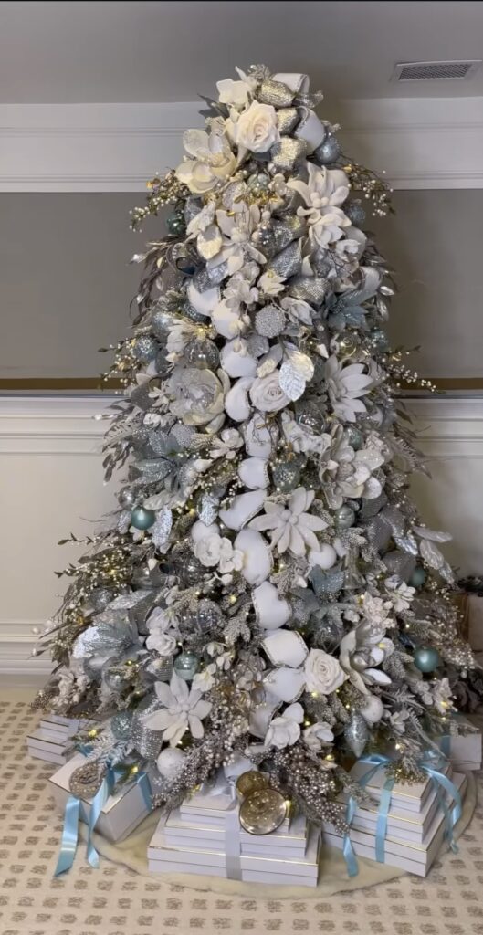 White-and-silver luxury winter wonderland tree with icy florals, pale blue accents, and stacked gift boxes.