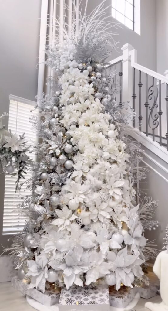 All-white winter wonderland poinsettia tree on a grand staircase with frosted foliage and pearl ornaments.