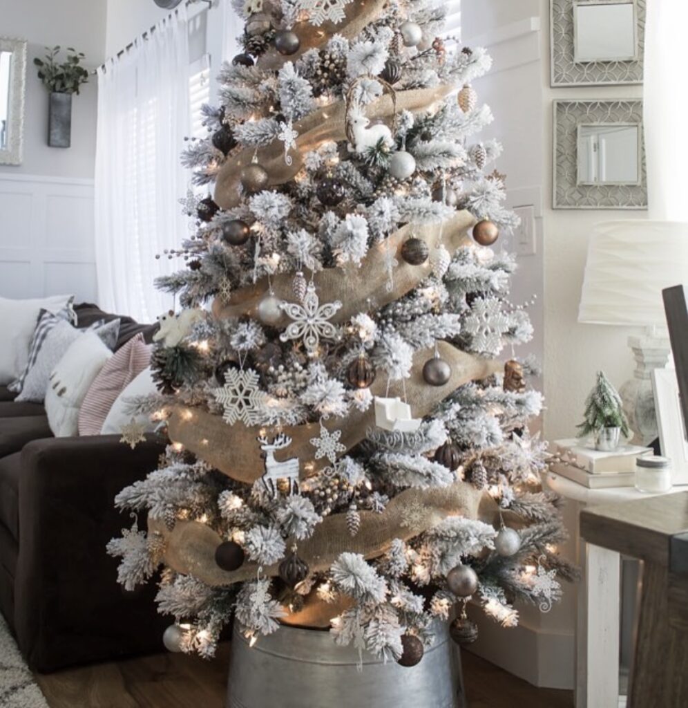 Farmhouse winter wonderland Christmas tree with burlap garland, frosted branches, and galvanized bucket base.