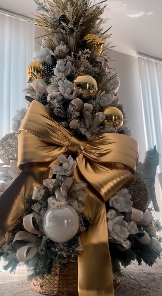 Gold Christmas tree decorated with oversized metallic bow with gold ornaments, ribbon, and warm white lights.