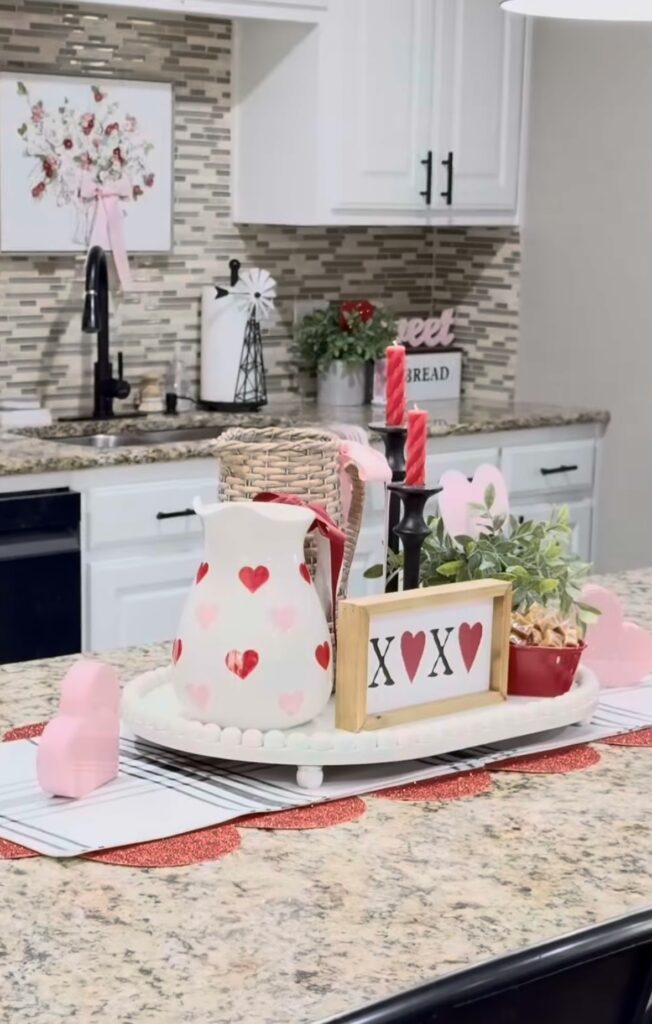 Kitchen tray styling with  a white pitcher with red and pink hearts, a sign with x's and hearts, a black candle holder with red candle on a wooden tray in a kitchen for valentines decorations