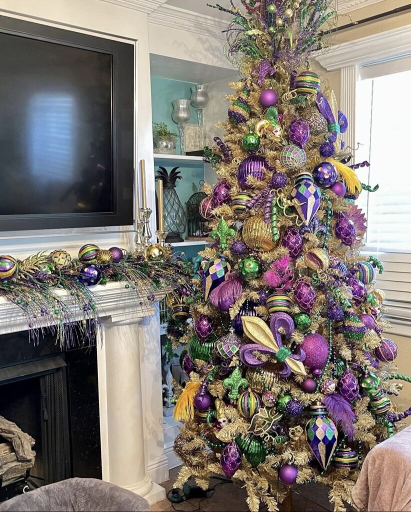 Gold Mardi Gras Christmas tree next to a living room fireplace, covered in purple, green, and gold ornaments with feathers, fleur-de-lis accents, and bead garland, plus a matching Mardi Gras mantel swag.