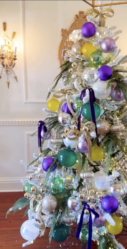 Close up of frosted Christmas tree with Mardi Gras colors, purple and green ornaments, and gold ribbon bows.