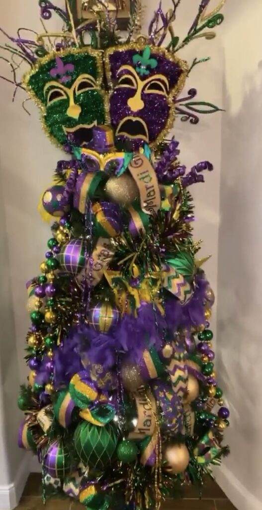 Mardi Gras Christmas tree with a jester mask topper, purple and green ornaments, and gold accents.