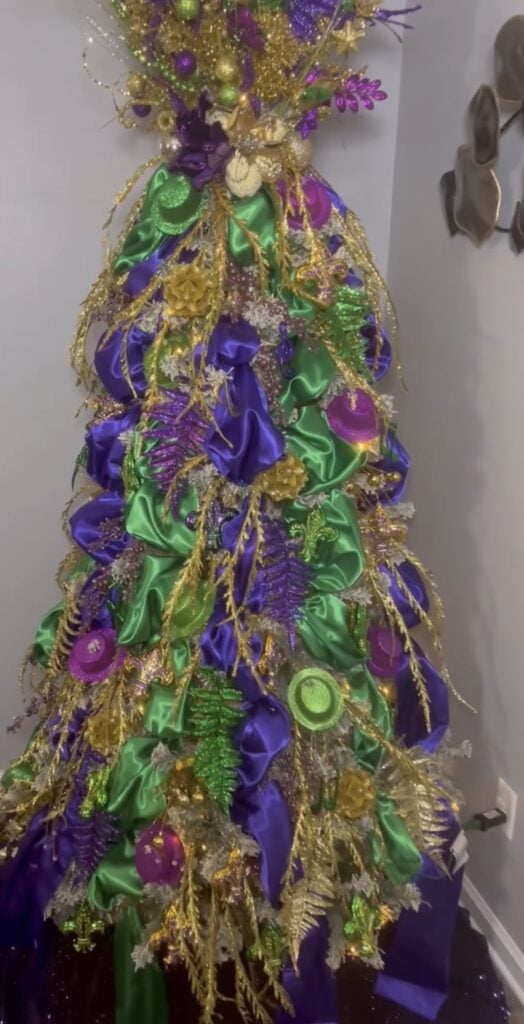 Mardi Gras Christmas tree wrapped in purple and green satin ribbon with gold sprays and glitter ornaments.