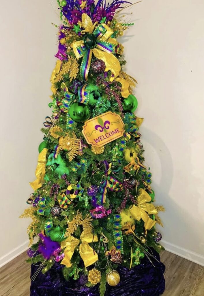 Mardi Gras Christmas tree with gold bows, purple and green ornaments, and a “Welcome” sign with a fleur de lis.