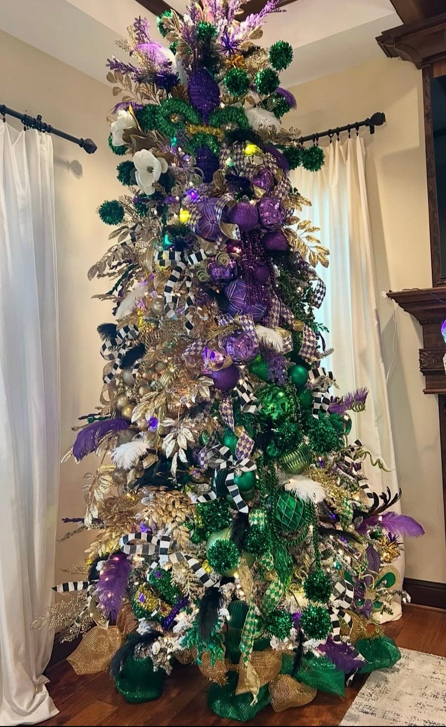 Glam Mardi Gras Christmas tree with purple and green ornaments, gold floral sprays, black and white check ribbon, and feather picks.