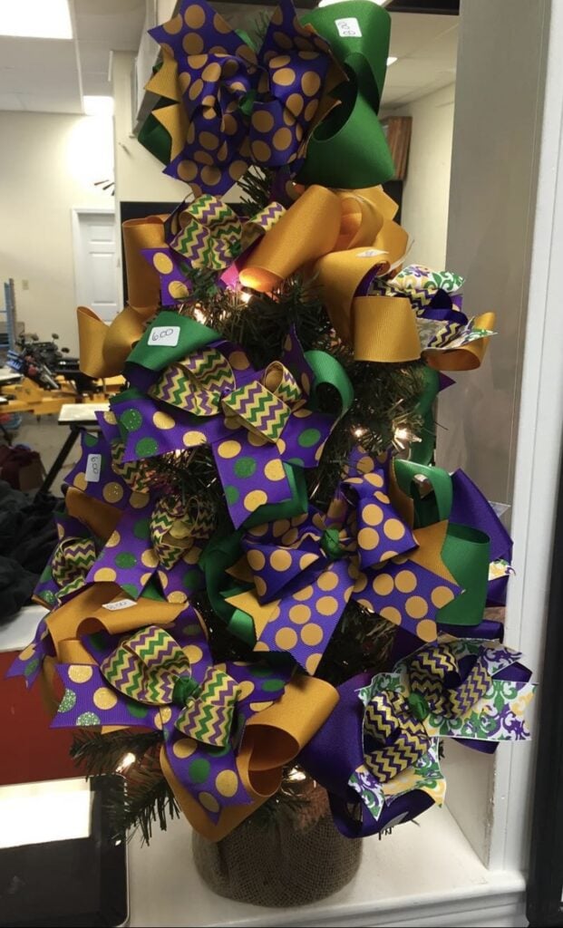 Small tabletop Mardi Gras tree wrapped in oversized purple, green, and gold bows with polka dot and chevron ribbon, lit with warm white lights.