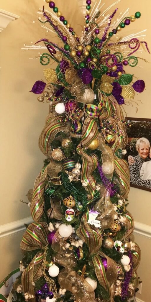 Classic Mardi Gras Christmas tree with wide gold mesh ribbon spirals, striped ornaments, bead sprays, and shiny purple and green ball ornaments.