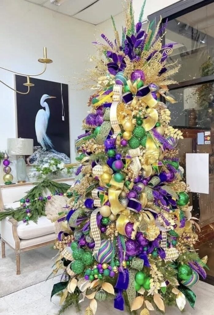 Mardi Gras themed Christmas tree in a styled living room display with layered gold ribbon, purple and green ornaments, and a tall feather-and-spray topper.