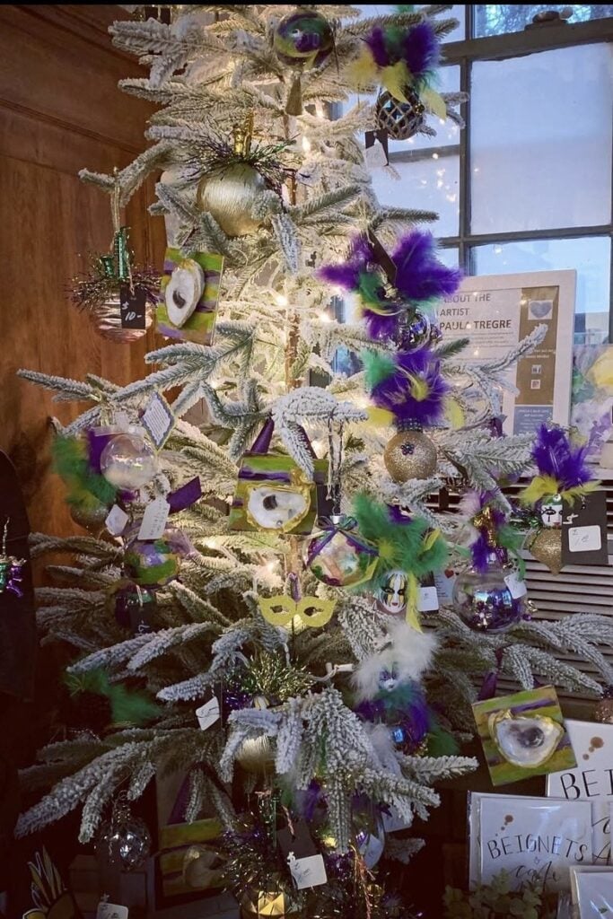 White flocked Mardi Gras tree decorated with feathered mask ornaments, oyster shell accents, glittery ball ornaments, and pops of purple and green.
