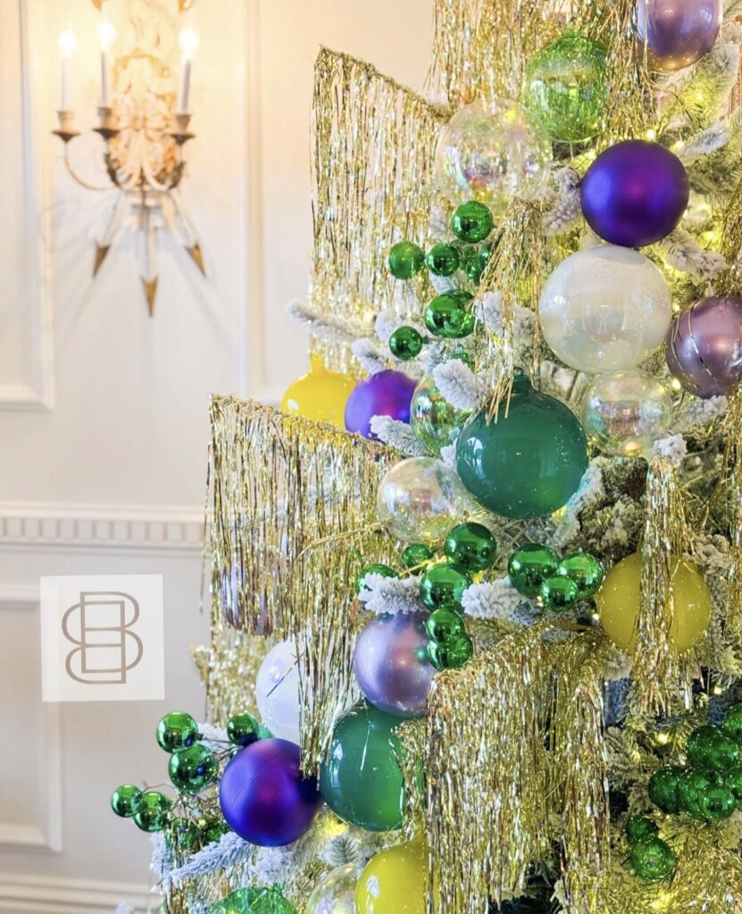 Close up of Mardi Gras tree with gold fringe garland, green bead picks, and purple, green, and gold ornaments.
